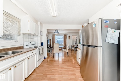Kitchen with freestanding refrigerator, white electric range, white cabinetry, a textured ceiling, and light wood-type flooring - 15515 92A Avenue, Edmonton, AB - Indoor Photo Showing Kitchen