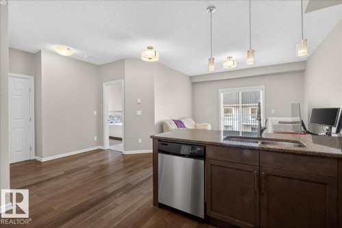 This open-concept living area features rich hardwood flooring, neutral wall tones, and a kitchen island with a built-in sink and stainless steel dishwasher - 413 2203 44 Avenue, Edmonton, AB - Indoor Photo Showing Kitchen