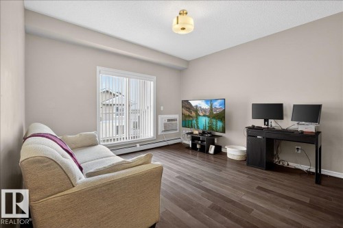 Living area featuring dark wood-style flooring, light-colored walls, and a window with vertical blinds - 413 2203 44 Avenue, Edmonton, AB - Indoor Photo Showing Living Room
