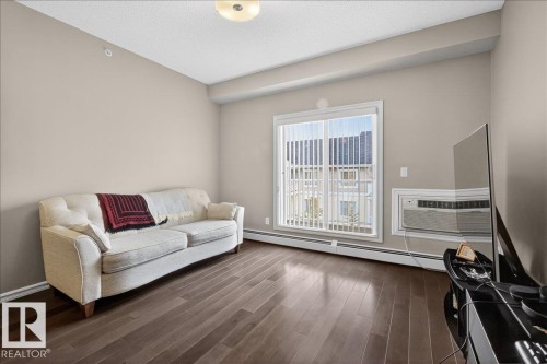 Living area featuring hard flooring, a large window with vertical blinds, and a wall-mounted air conditioning unit - 413 2203 44 Avenue, Edmonton, AB - Indoor