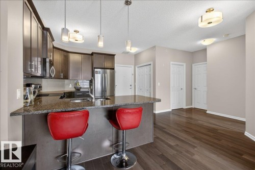 The kitchen features granite countertops, dark wood cabinetry, a stainless steel refrigerator, and pendant lighting - 413 2203 44 Avenue, Edmonton, AB - Indoor Photo Showing Kitchen With Stainless Steel Kitchen With Upgraded Kitchen