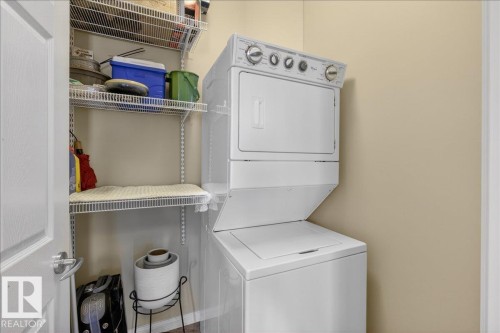 The property includes a laundry area with a white stacked washer and dryer unit, wire shelving for storage, and light-colored walls - 413 2203 44 Avenue, Edmonton, AB - Indoor Photo Showing Laundry Room