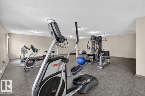 The property offers a fitness area with various exercise equipment, including an elliptical machine, stationary bike, treadmill, and a multi-station weight machine - 413 2203 44 Avenue, Edmonton, AB - Indoor Photo Showing Gym Room