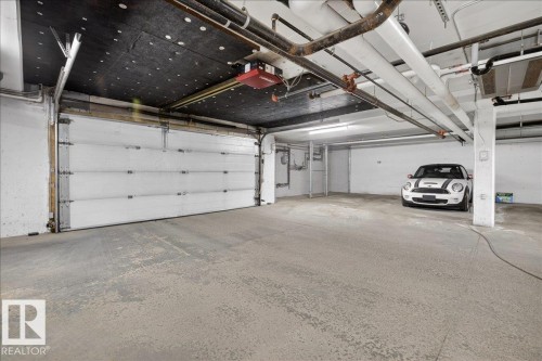 The property features a spacious garage with a large overhead door, concrete floors, and exposed ceiling utilities - 413 2203 44 Avenue, Edmonton, AB - Indoor Photo Showing Garage