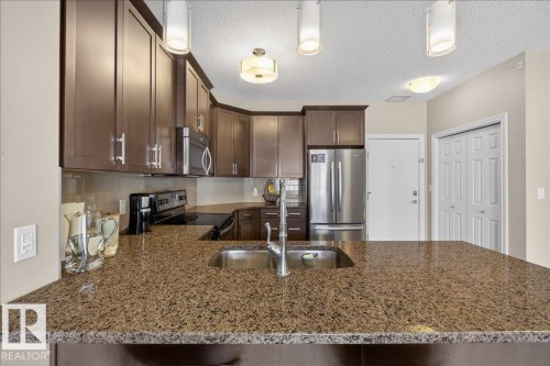 Kitchen featuring a double stainless steel sink, granite countertops, and dark wood cabinetry - 413 2203 44 Avenue, Edmonton, AB - Indoor Photo Showing Kitchen With Stainless Steel Kitchen With Double Sink With Upgraded Kitchen