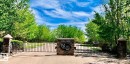 The property features a gated entrance with stone pillars, a paved driveway, and surrounding mature trees - 1-51025 Range Road 222, Rural Strathcona County, AB 