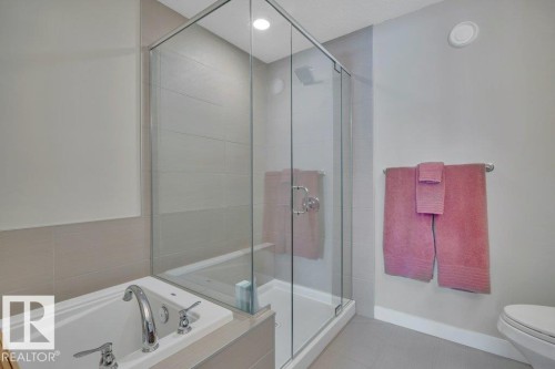 Bathroom featuring a tiled shower with a glass enclosure, a white bathtub with chrome fixtures, and light-colored wall and floor tiling - 9540 142 Street, Edmonton, AB - Indoor Photo Showing Bathroom