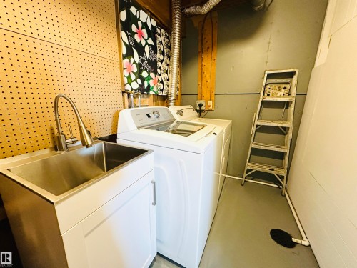 This utility area features a stainless steel sink with a modern faucet, white cabinetry, and a washer - 15 Pinecliff Close Ne, Calgary, AB - Indoor Photo Showing Laundry Room