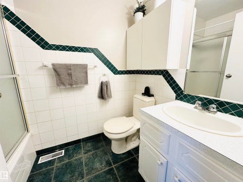 Bathroom with a vanity featuring a white countertop and integrated sink, a toilet, and tiled walls and flooring - 15 Pinecliff Close Ne, Calgary, AB - Indoor Photo Showing Bathroom
