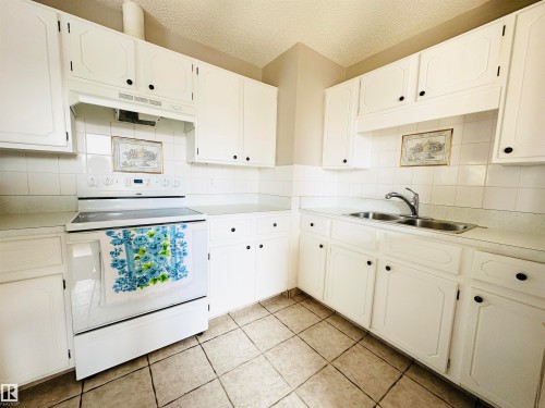 The kitchen features white cabinetry, a dual basin stainless steel sink, a range with an overhead vent, and tiled flooring - 15 Pinecliff Close Ne, Calgary, AB - Indoor Photo Showing Kitchen With Double Sink