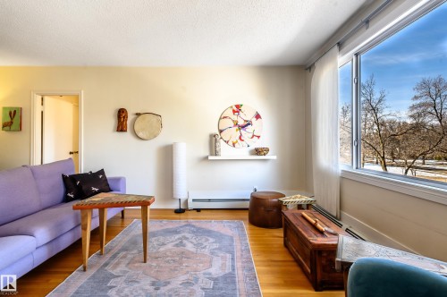 Living area featuring hardwood floors, a large window providing natural light, and a view of trees - 12 6805 112 Street, Edmonton, AB - Indoor