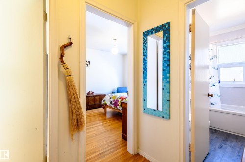 This hallway features light-colored walls and polished hardwood flooring, with a mirror mounted on one wall - 12 6805 112 Street, Edmonton, AB - Indoor Photo Showing Other Room