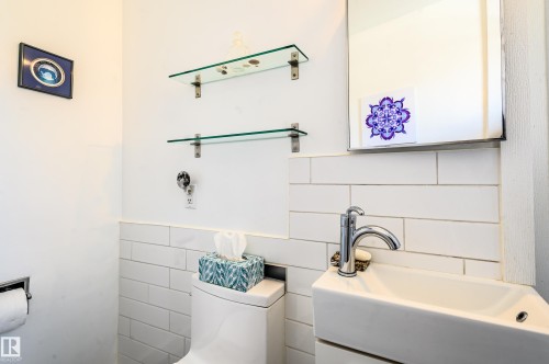 The bathroom features white subway tile wainscoting, a wall-mounted sink with a chrome faucet, and a toilet - 12 6805 112 Street, Edmonton, AB - Indoor Photo Showing Bathroom