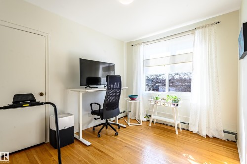 This room features hardwood floors and a bright window with white blinds and sheer curtains - 12 6805 112 Street, Edmonton, AB - Indoor Photo Showing Office