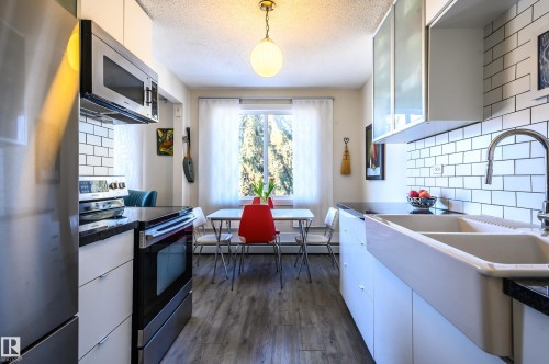 The kitchen features white subway tile backsplash, a stainless steel microwave, and white kitchen cabinets - 12 6805 112 Street, Edmonton, AB - Indoor Photo Showing Kitchen With Double Sink