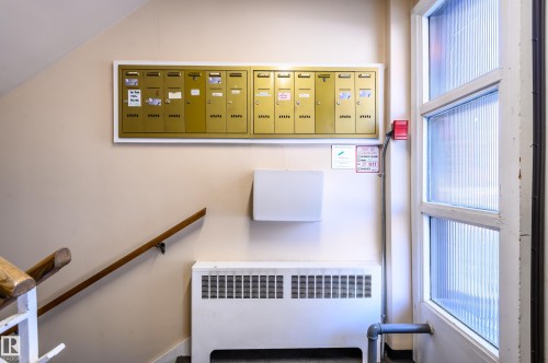 The property features a wall-mounted mailbox system, a wooden handrail along the staircase, and a white radiator - 12 6805 112 Street, Edmonton, AB - Indoor Photo Showing Other Room