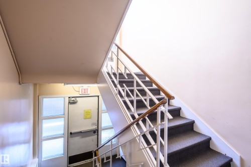 Stairwell featuring carpeted stairs, a white metal railing, and a wooden handrail - 12 6805 112 Street, Edmonton, AB - Indoor Photo Showing Other Room