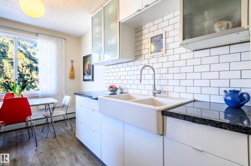The kitchen features a white farmhouse-style double sink, dark countertops, and a white subway tile backsplash - 12 6805 112 Street, Edmonton, AB - Indoor Photo Showing Kitchen With Double Sink