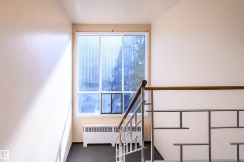 Entryway with a large window providing natural light, a baseboard heater, and a staircase with a wooden handrail and metal balusters - 12 6805 112 Street, Edmonton, AB - Indoor Photo Showing Other Room