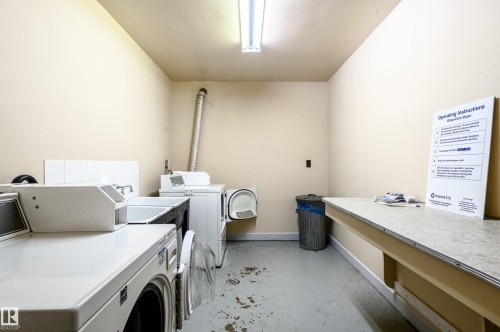 Dedicated laundry area featuring several washing machines and dryers, a utility sink, and a countertop for folding - 12 6805 112 Street, Edmonton, AB - Indoor Photo Showing Laundry Room