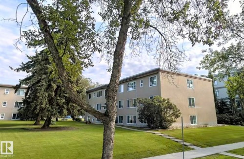 The property features a well-maintained lawn and mature trees, alongside a multi-story building with numerous windows - 12 6805 112 Street, Edmonton, AB - Outdoor