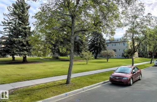 The property features a well-maintained lawn with mature trees and a paved sidewalk - 12 6805 112 Street, Edmonton, AB - Outdoor