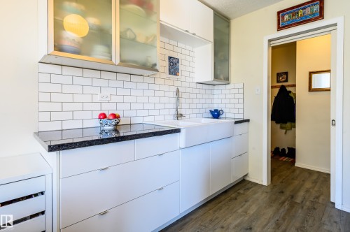 The kitchen features white subway tile backsplash, dark countertops, white cabinetry with a farmhouse sink, and frosted glass upper cabinets - 12 6805 112 Street, Edmonton, AB - Indoor