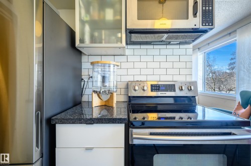 The kitchen features a stainless steel refrigerator, white subway tile backsplash, dark granite countertops, and a stainless steel oven with an overhead microwave - 12 6805 112 Street, Edmonton, AB - Indoor Photo Showing Kitchen