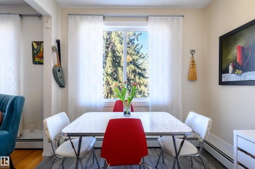 Dining area featuring a window with white curtains, a rectangular table, and hardwood flooring - 12 6805 112 Street, Edmonton, AB - Indoor Photo Showing Dining Room