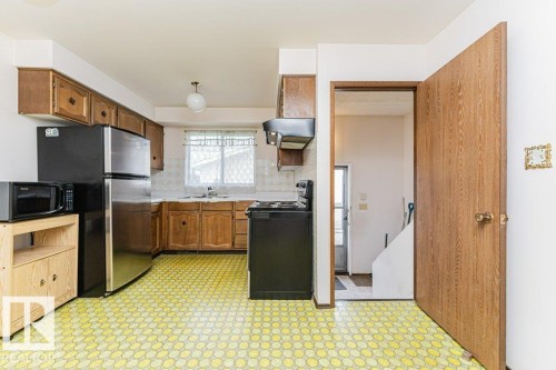 The kitchen features wooden cabinetry, a stainless steel refrigerator, and a window with natural light - 8804 19 Avenue, Edmonton, AB - Indoor Photo Showing Kitchen
