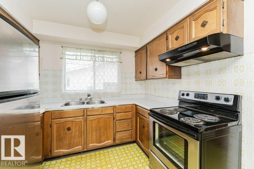Kitchen featuring wood cabinetry, a stainless steel electric stove, and a double basin sink beneath a window - 8804 19 Avenue, Edmonton, AB - Indoor Photo Showing Kitchen With Double Sink