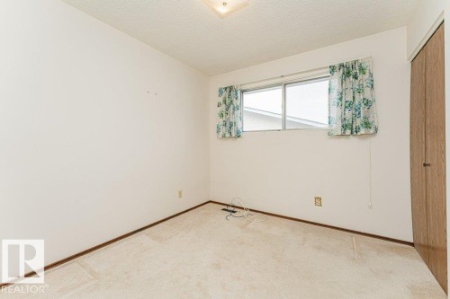 Bedroom featuring light-colored carpet, a window with floral curtains, and a built-in closet with a wooden door - 8804 19 Avenue, Edmonton, AB - Indoor Photo Showing Other Room