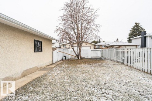 The property includes a spacious backyard with a white picket fence, a mature tree, and a paved pathway leading to the rear of the home - 8804 19 Avenue, Edmonton, AB - Outdoor