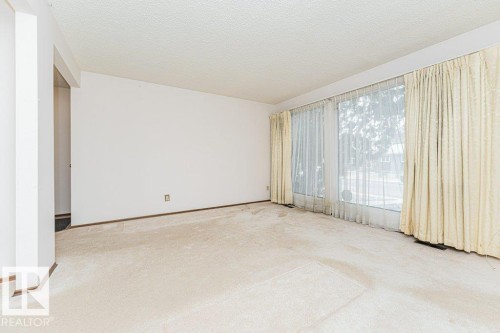 Spacious living area featuring large windows with sheer and opaque curtains, neutral wall tones, and carpeted floors - 8804 19 Avenue, Edmonton, AB - Indoor Photo Showing Other Room
