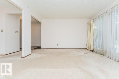 Living area featuring light-colored carpeting, white walls, and a large window with sheer and opaque curtains - 8804 19 Avenue, Edmonton, AB - Indoor Photo Showing Other Room