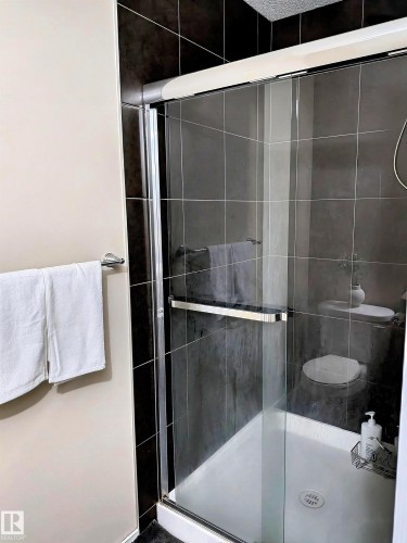 This bathroom features a shower with sliding glass doors and dark tiled walls, complete with a white shower base - 225 51A Street, Edmonton, AB - Indoor Photo Showing Bathroom