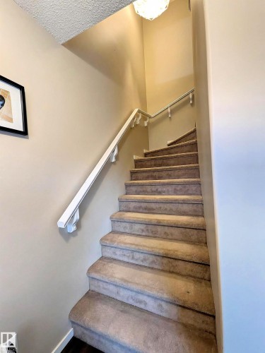 The staircase features carpeted steps and a white handrail, complemented by a decorative light fixture overhead - 225 51A Street, Edmonton, AB - Indoor Photo Showing Other Room