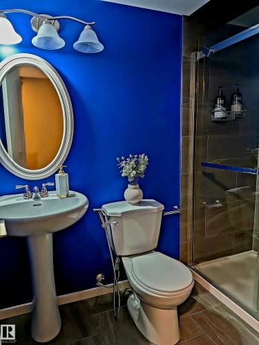 The bathroom features a pedestal sink with a chrome faucet, an oval mirror, and a shower enclosure with glass doors - 225 51A Street, Edmonton, AB - Indoor Photo Showing Bathroom