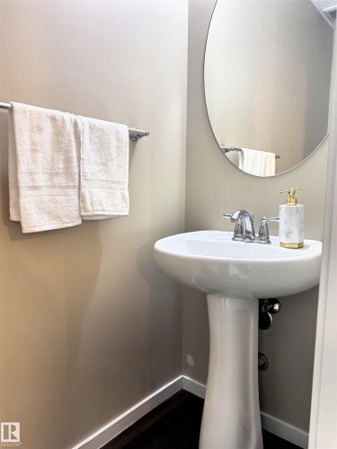 Bathroom featuring a white pedestal sink with chrome faucet, a circular wall-mounted mirror, and dark flooring - 225 51A Street, Edmonton, AB - Indoor Photo Showing Bathroom