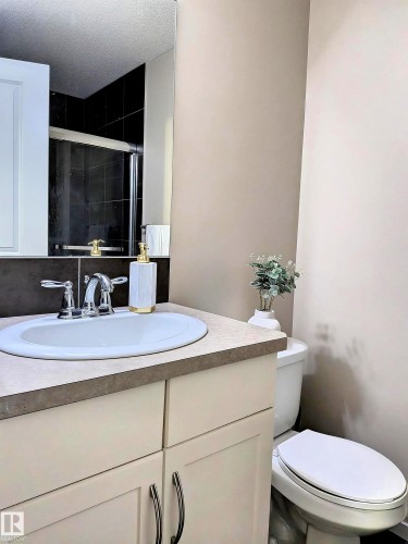 Bathroom featuring a white oval sink with chrome faucet, a light-colored vanity with dark hardware, a toilet, and a large wall mirror - 225 51A Street, Edmonton, AB - Indoor Photo Showing Bathroom