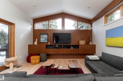 Living area featuring light wood flooring, a built-in media console with wood paneling, and an expansive window with a view of trees - 