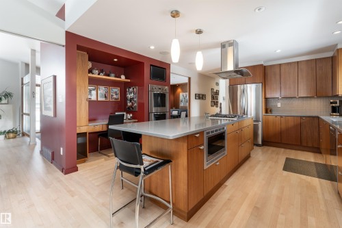 The kitchen features light wood flooring, a central island with a built-in microwave, and stainless steel appliances including a refrigerator, oven, and range hood - 9715 141 Street Nw, Edmonton, AB - Indoor Photo Showing Kitchen With Upgraded Kitchen