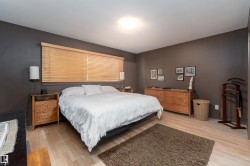 Bedroom featuring light-toned flooring, a window with blinds, and walls painted in a dark neutral tone - 