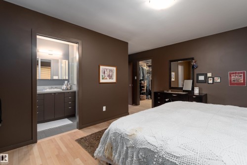 The bedroom features hardwood flooring and direct access to a bathroom with a vanity and mirror, and a walk-in closet - 9715 141 Street Nw, Edmonton, AB - Indoor Photo Showing Bedroom