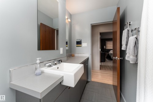 The bathroom features a vanity with a white rectangular sink, a large mirror, and light gray walls - 9715 141 Street Nw, Edmonton, AB - Indoor