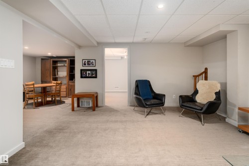 The property features a spacious room with light-colored carpet, a drop ceiling with recessed lighting, and a wooden staircase - 9715 141 Street Nw, Edmonton, AB - Indoor