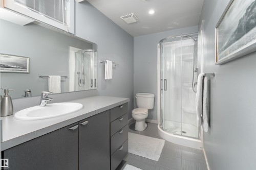 Bathroom featuring a vanity with a white oval sink and chrome faucet, a large mirror, and a curved glass shower enclosure - 9715 141 Street Nw, Edmonton, AB - Indoor Photo Showing Bathroom