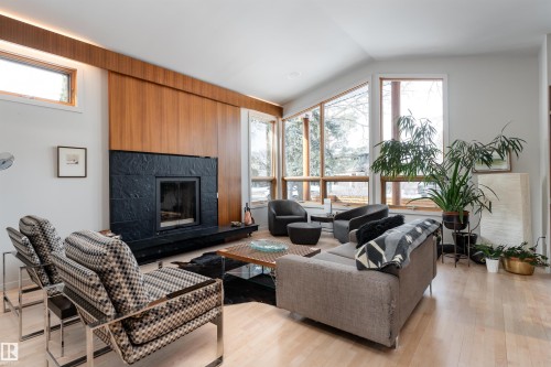 The living area features hardwood floors and a striking fireplace with a dark stone surround and hearth - 9715 141 Street Nw, Edmonton, AB - Indoor Photo Showing Living Room With Fireplace