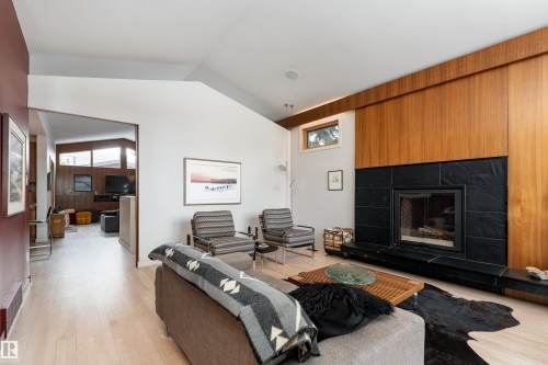 Living area featuring light-toned flooring, a fireplace with a black stone surround, and wood paneling - 9715 141 Street Nw, Edmonton, AB - Indoor Photo Showing Living Room With Fireplace