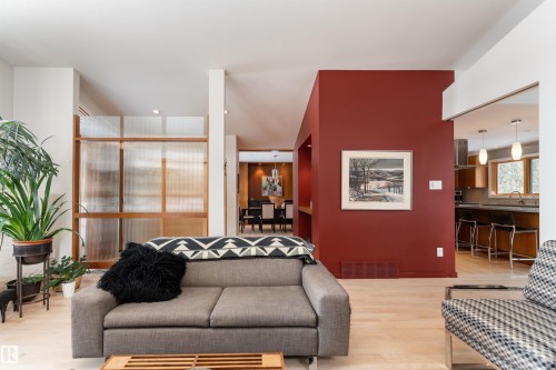 The property features light-toned flooring, a red accent wall, and a wooden room divider - 9715 141 Street Nw, Edmonton, AB - Indoor Photo Showing Living Room